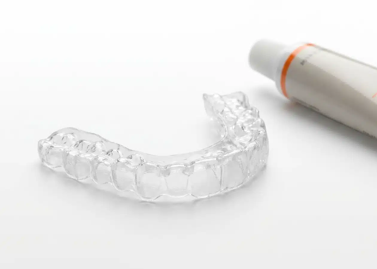 Moldeira individualizada transparente para clareamento dental supervisionado em casa, ao lado de seringa com gel clareador