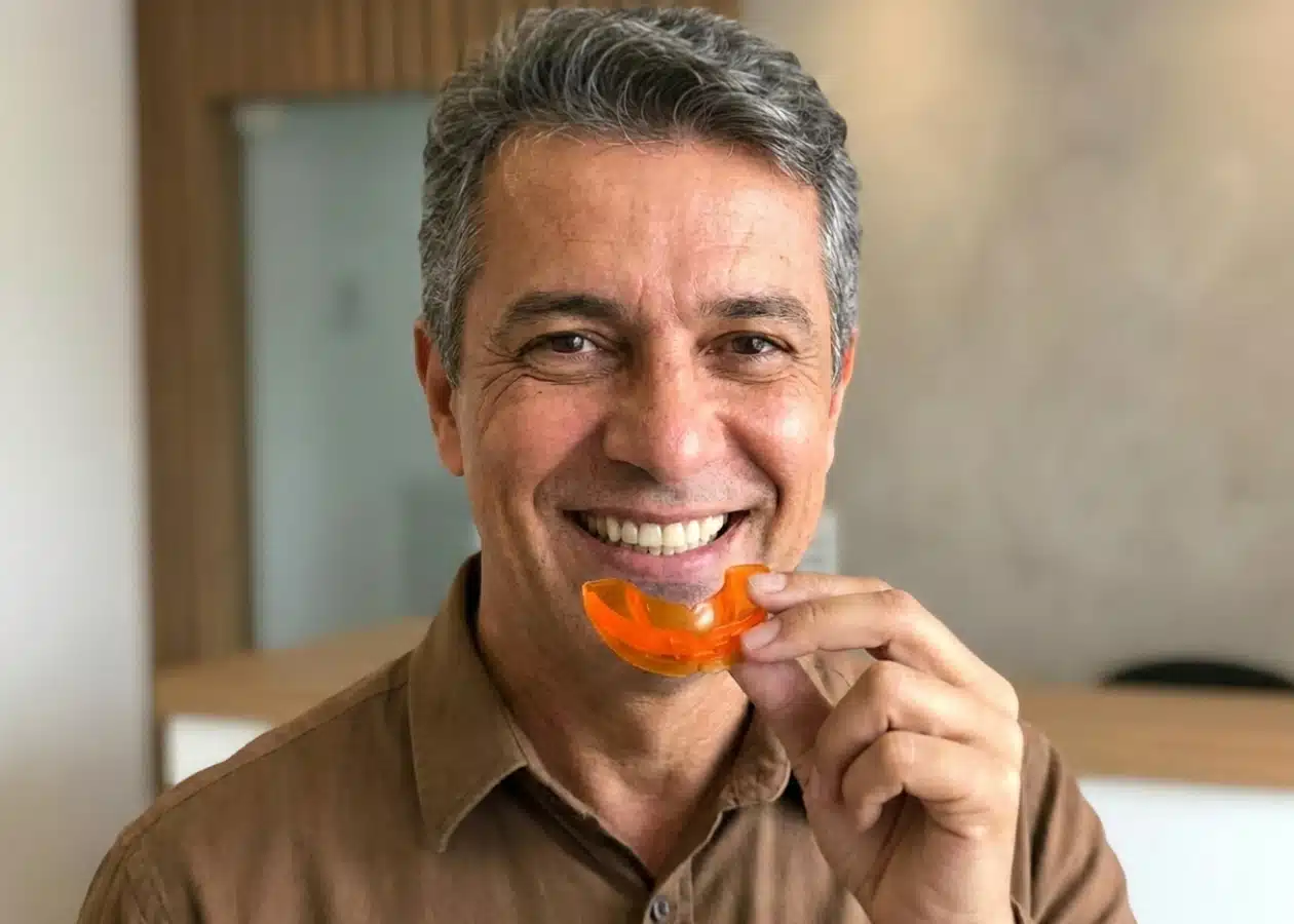 Paciente sorrindo segurando placa miorrelaxante noturna laranja de proteção contra bruxismo